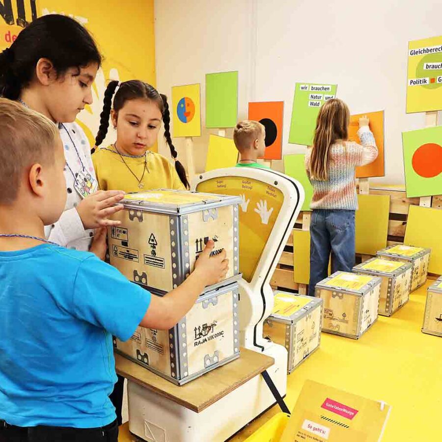 Drei Kinder probieren im Museum die Klimawaage aus.